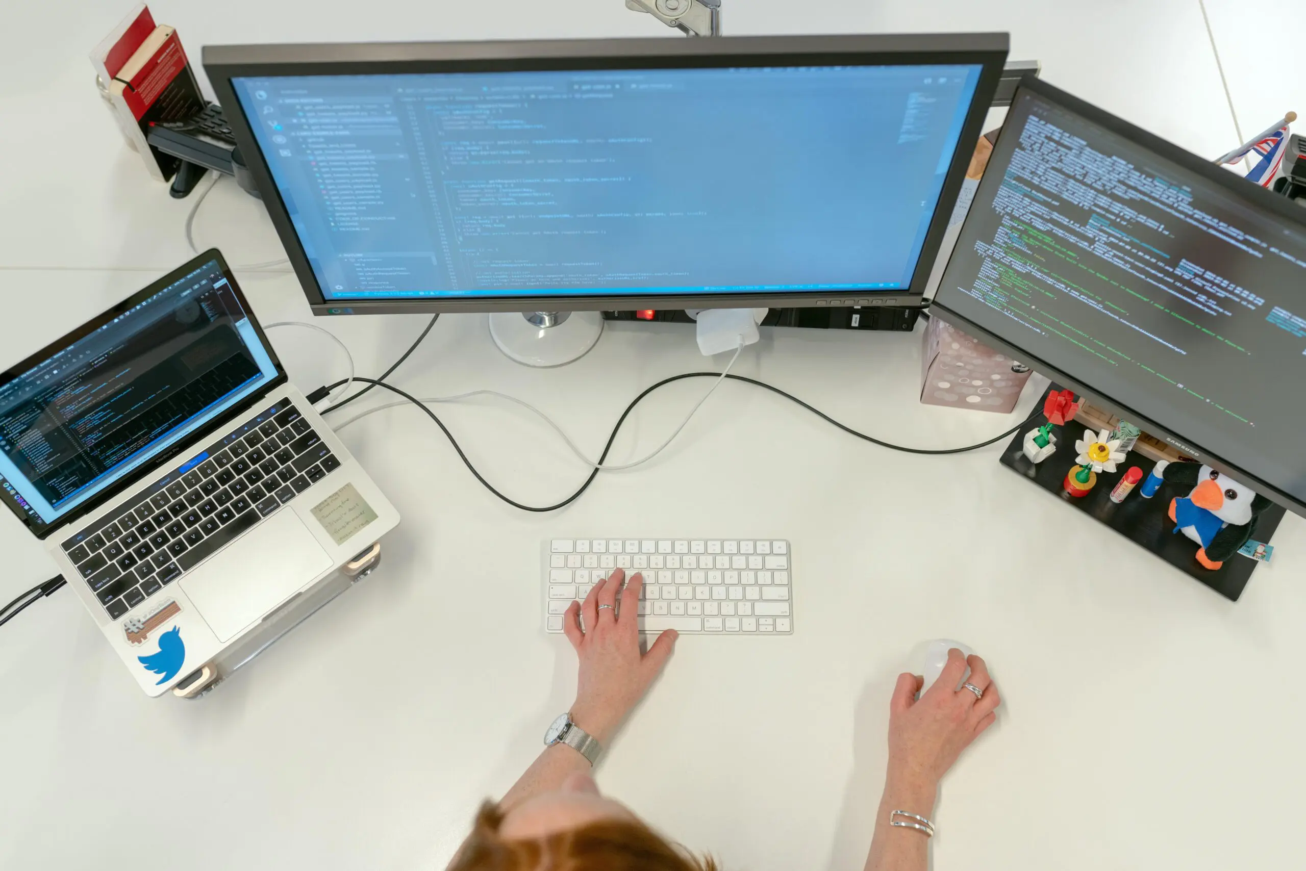 Workspace with a person coding on a laptop and dual monitors, surrounded by desk accessories.