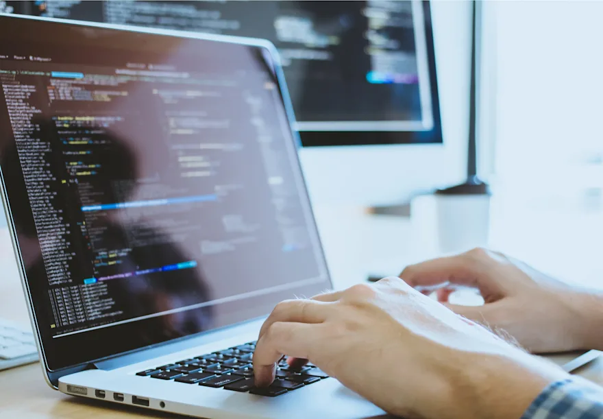 
                        A person coding on a laptop with a screen displaying programming code